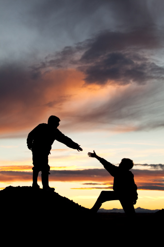 Concept image of two boys climbing a hill with one reaching out to help the other. Silhouette. Elementary age children. Side view. Teamwork concept. This image of two unrecognizable boys could also be used for other themes such as: courage, friendship, togetherness, help, encouragement, support, difficulties, care, teamwork, moving forward, and so on. 