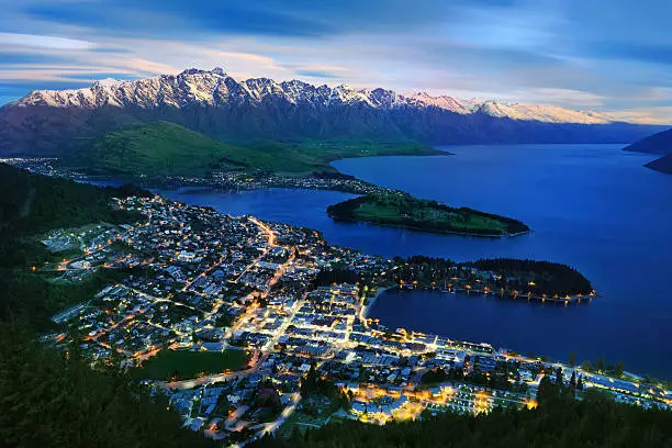 Queenstown at dusk, Otago, New Zealand. Spring has just started and the peaks of the alps in back got their last powder snow. The last sunlight adds a warm tone to the mountain range while Queenstown is already brightly illuminated by the street lights. Nikon D3X. Converted from RAW.