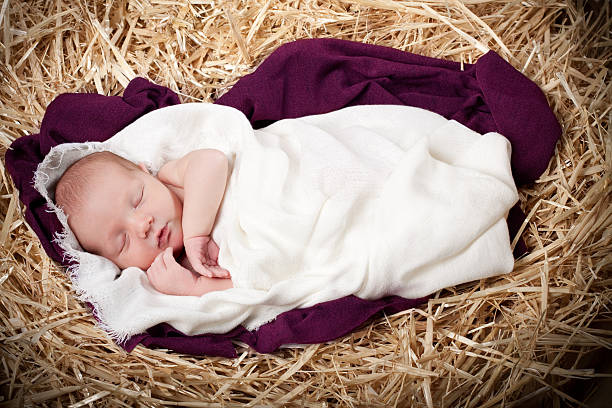 Nativity with Baby Sleeping in Manger Nativity scene with a newborn baby boy wrapped in a woven blanket on top of a purple blanket, sleeping in a manger. bed of hay stock pictures, royalty-free photos & images