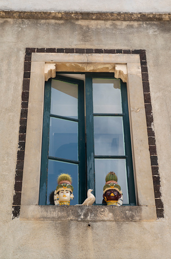 Old wooden open window with two ceramic pots in the shape of man heads and a dove in Sicilia, Italy, Europe