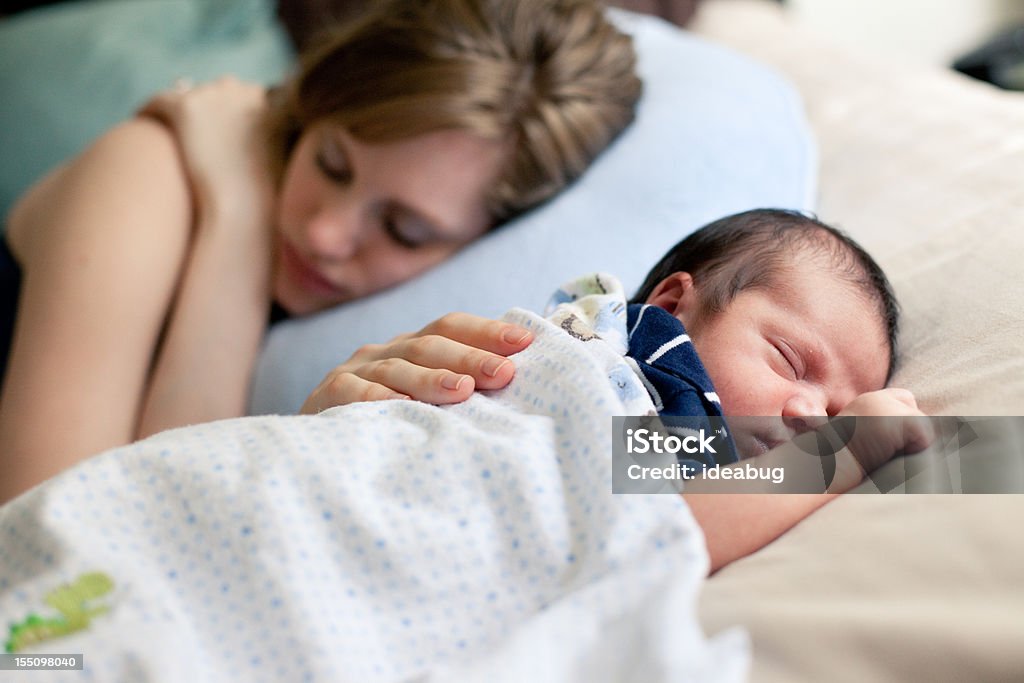 Mother and Newborn Sleeping Peacefully on Bed Together Close up color image of a loving sleeping mother touching her sleeping mixed race newborn baby boy. (Note: Some grain due to use of higher ISO, limited available natural light while they were sleeping) Sleeping Stock Photo