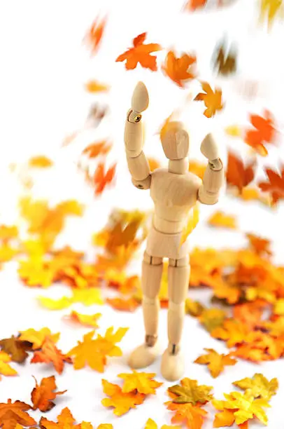 Wooden mannequin enjoying falling down autumn leaf. hands raising into the air. soft focos on head and hands. autumn background.