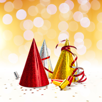 Party decorations: hats, whistles, streamers, confetti on white background. Square composition, golden lights background.