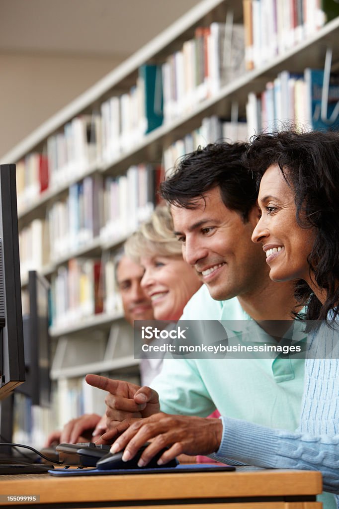 Studenti che lavorano su computer in libreria - Foto stock royalty-free di Adulto