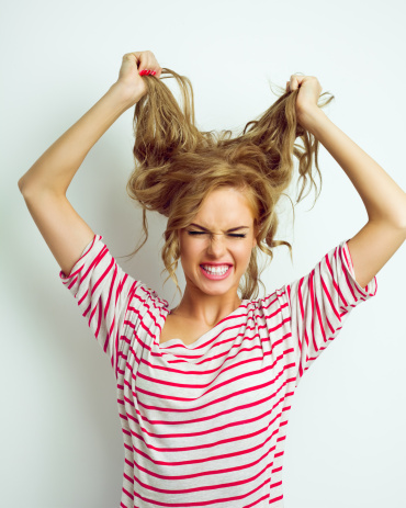 Portrait of frustrated young woman tearing her hair out and screaming. Studio shot, white background.