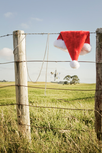 A Santa hat and Christmas decorations on a rustic, rural fence during summer in New Zealand.  Taken in December.