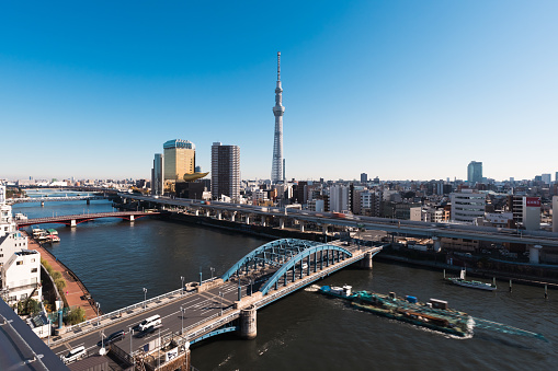 Cityscape view of Tokyo Skytree, ship and boat sail on Sumida River, car traffic transportation on highway road, bridge in Asakusa district, Japan. Asia travel landmark, Asian people city life concept