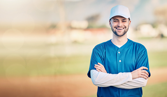 Portrait, smile and mockup with a baseball man standing arms crossed outdoor on a sports pitch. Fitness, training and happy with a young male athlete posing next to blank mock up space on a field