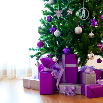Wrapped gifts under the Christmas tree in a bright interior with garland lights in bokeh.