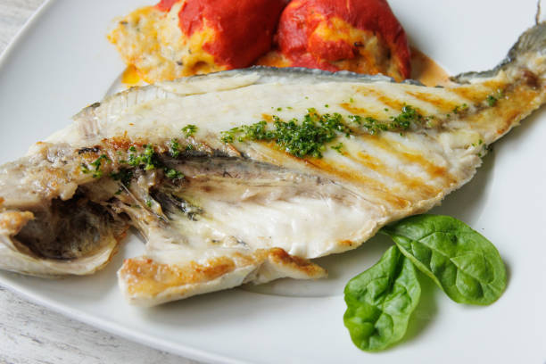 istock Grilled gilt-head bream on a white plate accompanied by stuffed piquillo peppers 1551003513