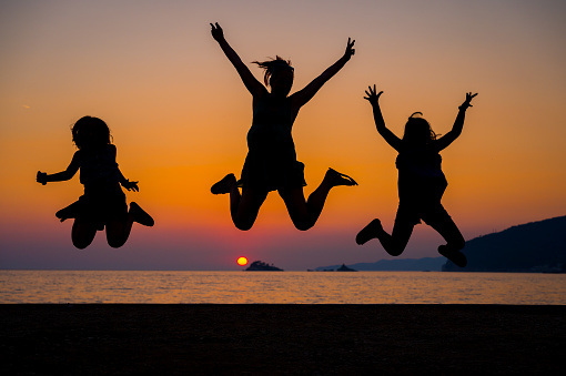 Silhouette of mother and children jumping at sunset on a beach. People jumping with hands raised on a sunset beach with the sea in the background. Amazing sunset in the Adriatic sea.