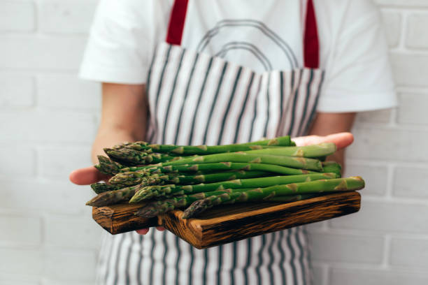 Female hands hold asparagus in a wooden tray close-up in daylight Female hands hold asparagus in a wooden tray close-up in daylight. Healthy food. Front view eating asparagus stock pictures, royalty-free photos & images