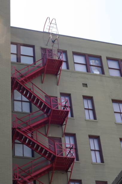 istock Red iron fire escape staircase leading to a second story window against a brick building wall 1551103491