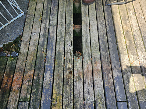 A small porch hole where a board has been removed from the deck.