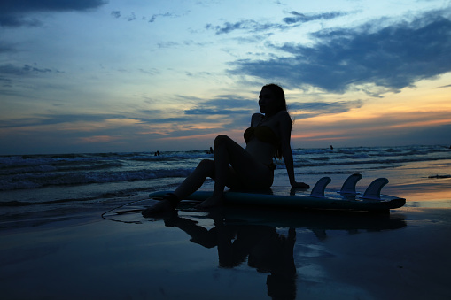 Silhouette woman sitting relax on surfboard  on twilight time in the evening