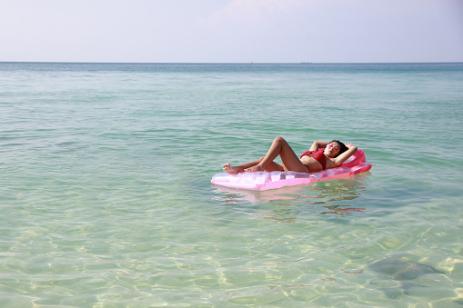 Young pretty woman lying down sunbathing on a float swimming seat