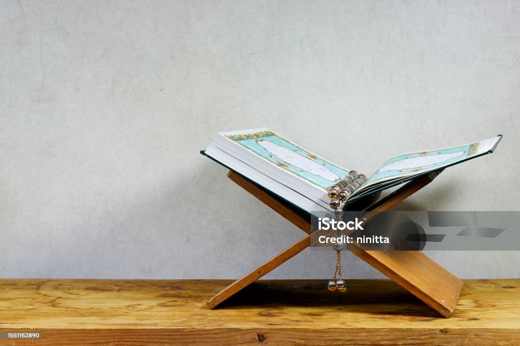 Mawlid al nabi or ramadan, eid concept.  muslim book with Arabic calligraphy Quran - translation : the noble book of Muslims around the world on stand and rosary on wooden board Koran Stock Photo