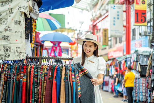 fashionable Asian woman, walking in Pealing Steet o Chinatown district in Kuala Lumpurt, shopping through market stalls.