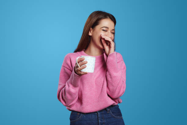 istock Brunette woman with shy expression smiles pleasantly with closed eyes while holding cup of coffee 1551163022