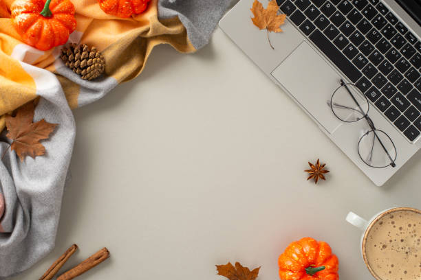 istock Top-down perspective encapsulates the working-from-home concept, featuring a laptop, cozy elements like blanket, pumpkins, pinecones, spices, glasses, coffee on isolated grey background and copyspace 1551169398