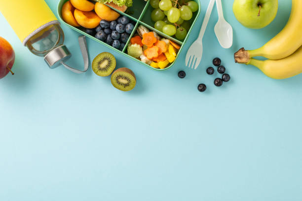 istock Boost your mental fuel: Vertical composition capturing a lunch box with sandwiches, fruits, vegetables and a water bottle on a pastel blue backdrop, providing space for text or promotional content 1551173828