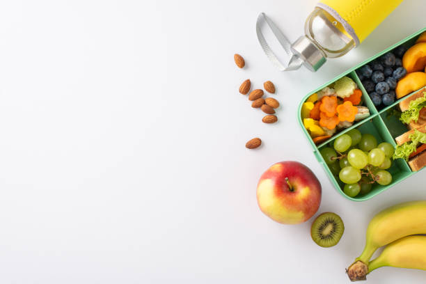 istock Showcase school lunch experience with a top-down image of lunchbox brimming with sandwiches, nutritious fruits, veggies and water bottle on white isolated background, offers space for text or adverts 1551175953