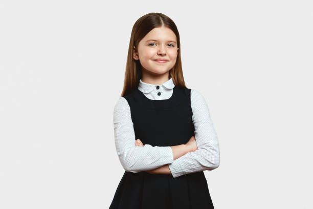 istock Smart focused schoolgirl in uniform looking at camera while standing alone, with arms crossed 1551175956