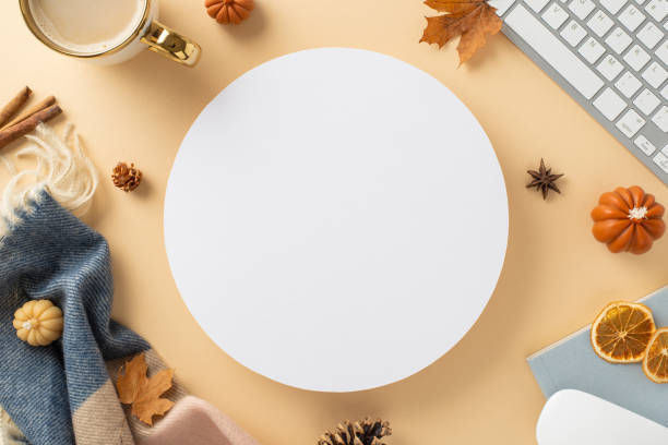istock Autumn-themed workplace at home. Top view image of laptop keyboard and mouse, notepad, mug of coffee, scarf, autumnal decorations with space for promotion inside of circle on beige isolated background 1551177153