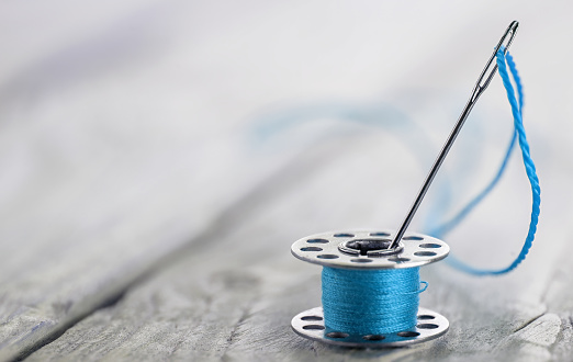 sewing bobbin with blue thread and needle