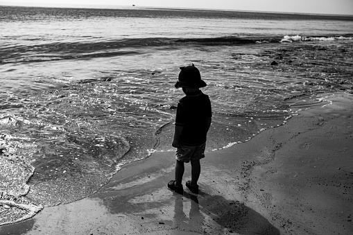 Young boy in greyscale at the beach watching the waves rolling under his feet