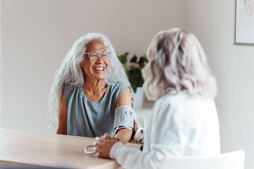 Vibrant and healthy multiracial senior woman of Hawaiian and Chinese descent smiles as her doctor measures her blood pressure at a routine medical appointment.