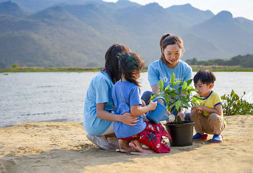 female volunteer joins planting tree with kids and teen by the river in community to instill awareness in kids to understand the basics of forest protection,natural resources conservation in earth day