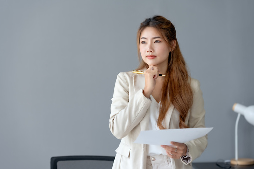 Beautiful young business woman manager or company worker holding accounting document, checking financial data or marketing report working in office with laptop. Accountant consults on some docum.