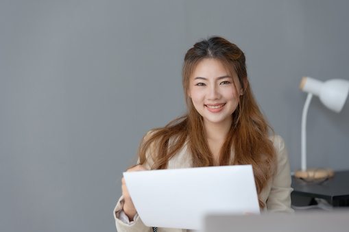 Beautiful young business woman manager or company worker holding accounting document, checking financial data or marketing report working in office with laptop. Accountant consults on some docum.