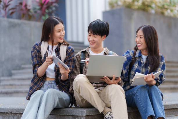 istock Group Of Young Asian Students Collaborating Outdoors at University. Teamwork and Knowledge Sharing. Asian Students Engaged in Collaborative Learning Outdoors. 1551209683