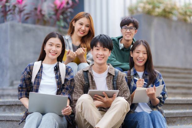 Group Of Young Asian Students Collaborating Outdoors at University. Teamwork and Knowledge Sharing. Asian Students Engaged in Collaborative Learning Outdoors.