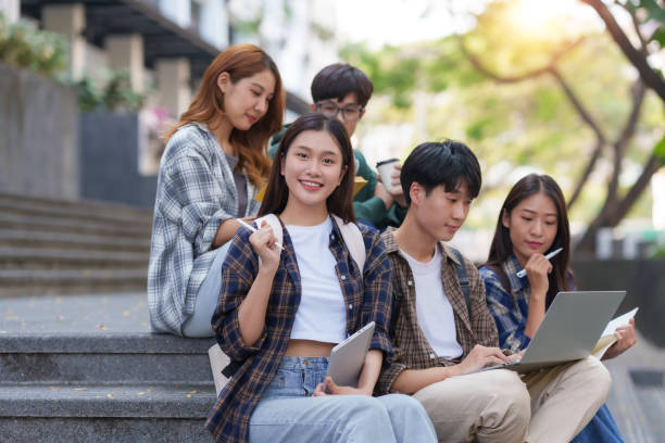 istock Group Of Young Asian Students Collaborating Outdoors at University. Teamwork and Knowledge Sharing. Asian Students Engaged in Collaborative Learning Outdoors. 1551209690