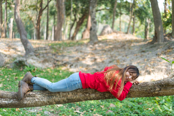 Happy beautiful woman lying down on a tree trunk in nature in red hoodie