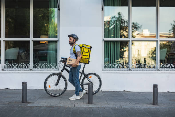 istock delivery man with his backpack riding a bicycle through the city with a package in his hand 1551211082