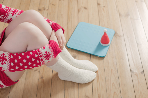 Female feet near  blue electronic scales for weight control  with Christmas santa hat on wooden floor
