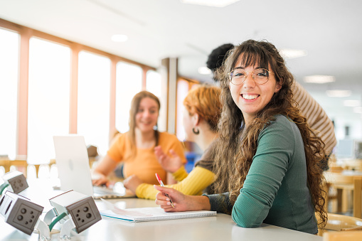 Group of students sitting studying in university library, girl with glasses smiling