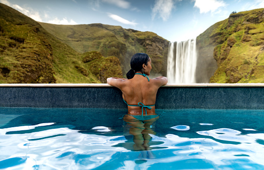 Rear view of an African American woman in a swimming at a hotel watching a beautiful waterfall