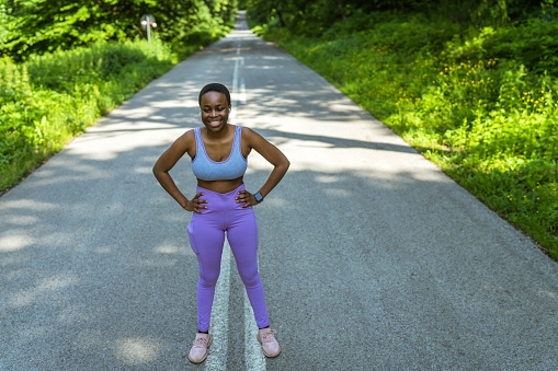 Woman athlete in running gear posing on empty road. Athlete standing on road early in the morning.