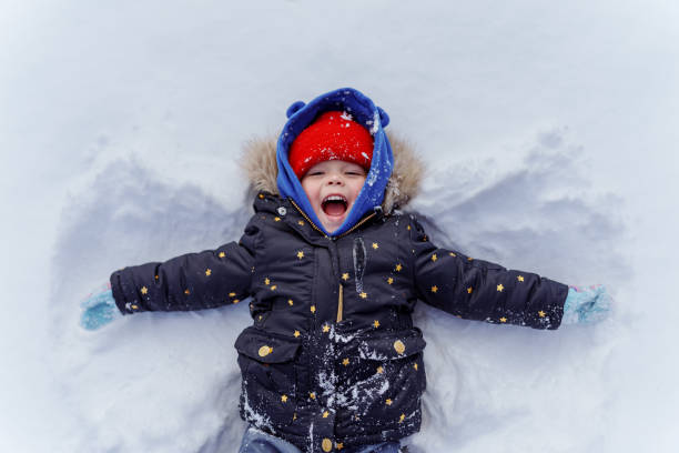 une jeune fille allongée dans la neige en train de faire un ange des neiges - child winter snow asian ethnicity photos et images de collection