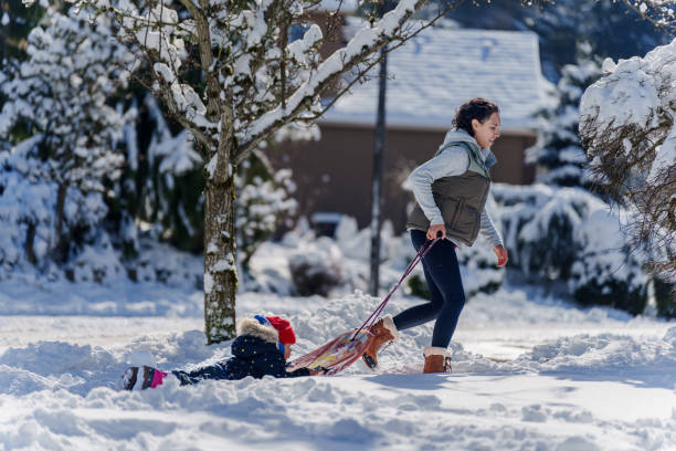 Young mother pulling daughter on a sled during snow storm