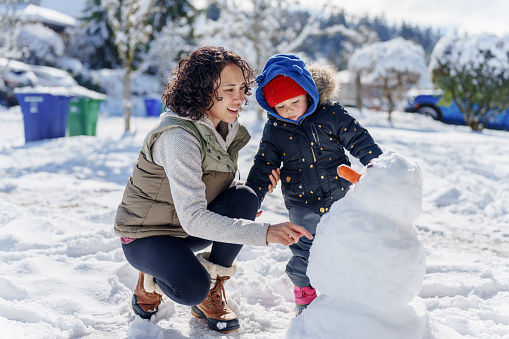 Young mother and daughter build a snowman outside