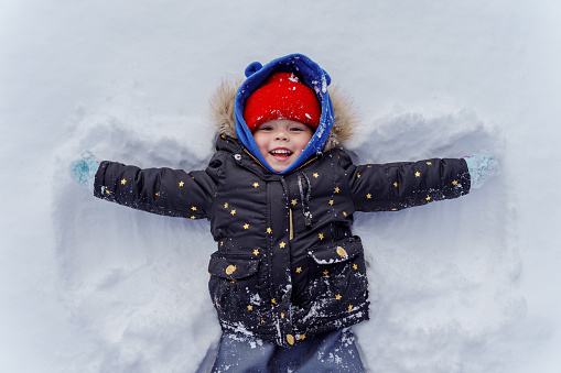 Young girl lays in snow making a snow angel