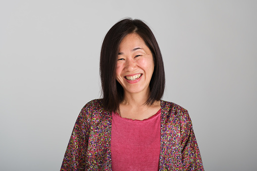 front view portrait of a beautiful and carefree Japanese female with pink t-shirt smiling in a white studio background