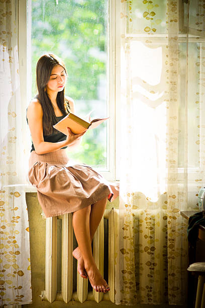istock Young woman reading book on window-sill 155124534