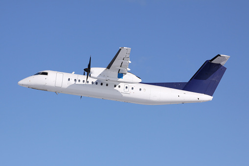 White / blue colored Bombardier Q300 / De Havilland Dash 8-300 departure with blue sky in the background. All trademarks are removed.
